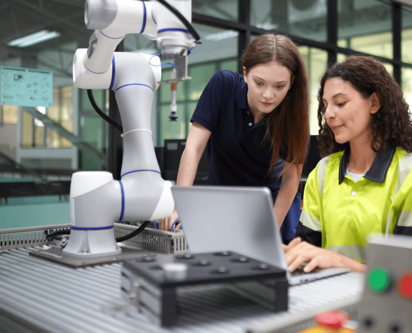 Brazo robótico programado Las dos mujeres están trabajando juntas, en un proyecto de robótica o ingeniería, utilizando la computadora para programar o monitorear el brazo robótico.