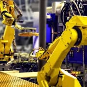 Sistema de automatización robótica, con dos brazos robóticos industriales de color amarillo en un entorno de fábrica