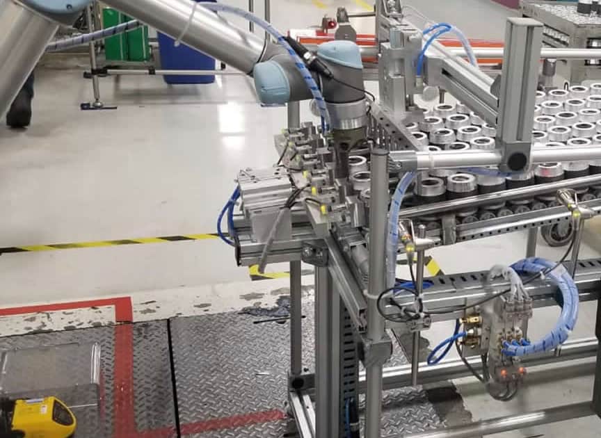 Línea de producción automatizada en una fábrica. Específicamente, se observa un sistema de embalaje que incluye un brazo robótico y una cinta transportadora con varias latas