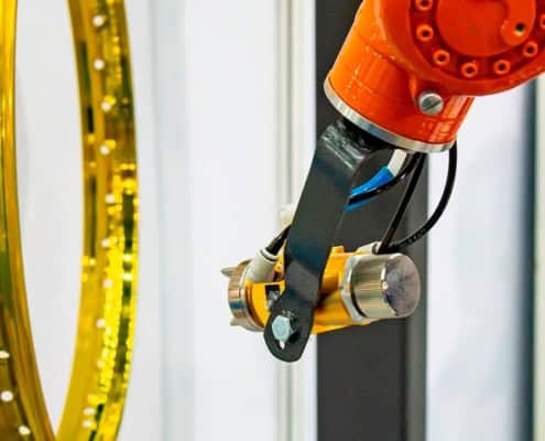 Brazo robótico industrial que está pintando un rin de motocicleta de color dorado