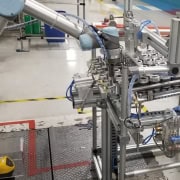 Línea de producción automatizada en una fábrica. Específicamente, se observa un sistema de embalaje que incluye un brazo robótico y una cinta transportadora con varias latas